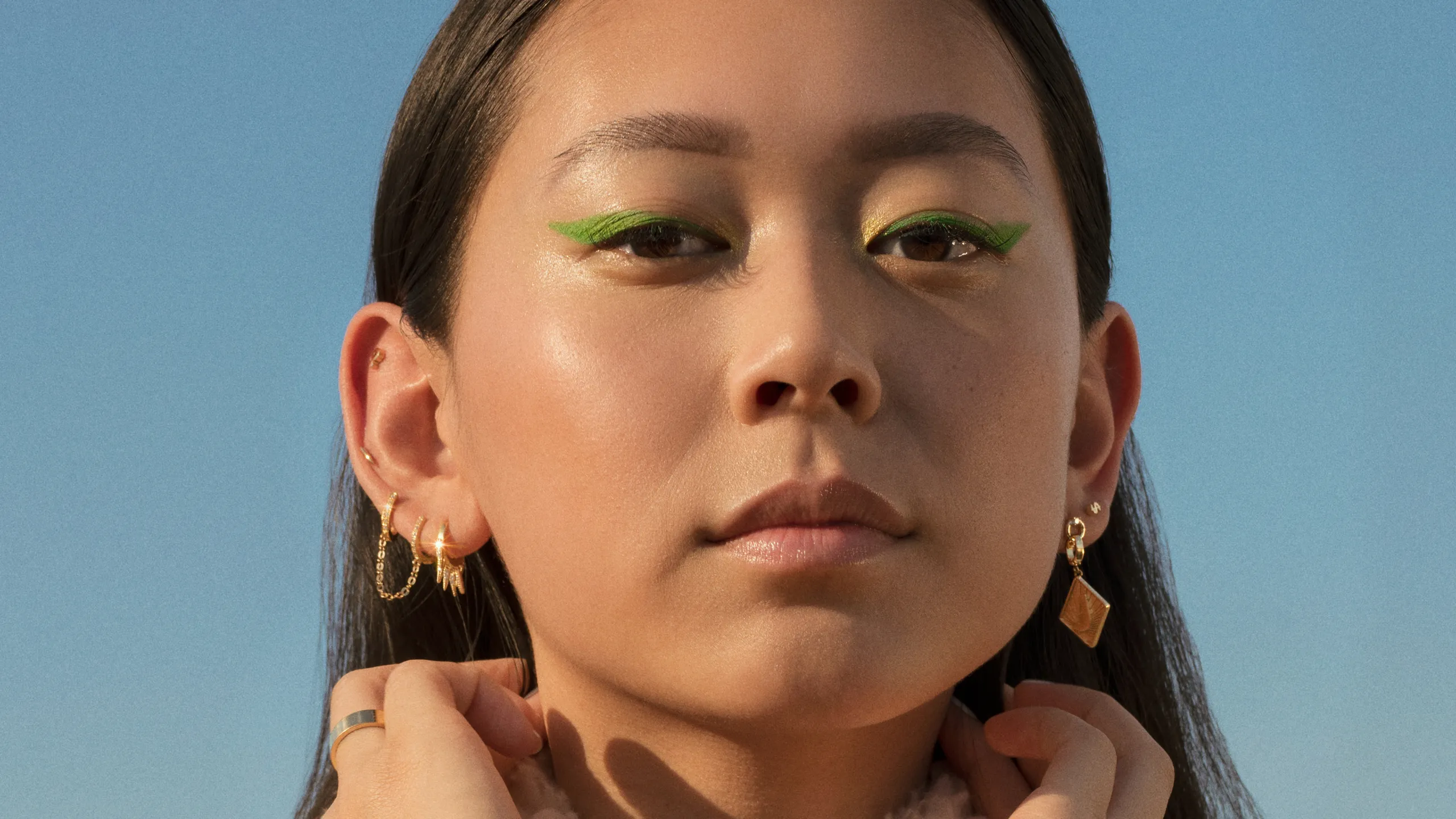 Woman with green eye makeup against a clear blue sky